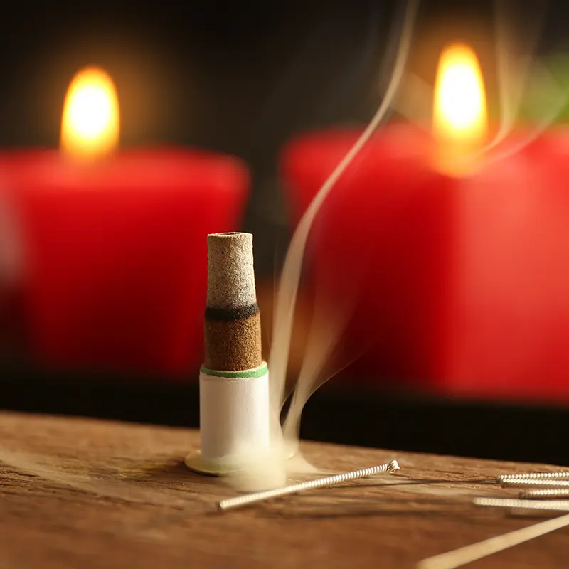 Traditional moxibustion therapy setup with burning moxa cone, acupuncture needles, and candles for relaxation and energy healing